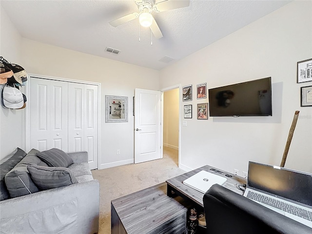 living area featuring a ceiling fan, visible vents, baseboards, a textured ceiling, and light colored carpet