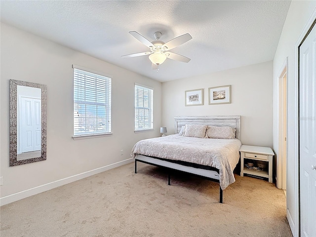 bedroom featuring baseboards, light carpet, a textured ceiling, and ceiling fan