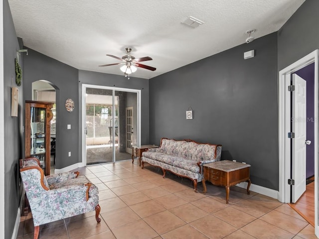 sitting room featuring visible vents, a textured ceiling, light tile patterned floors, baseboards, and ceiling fan