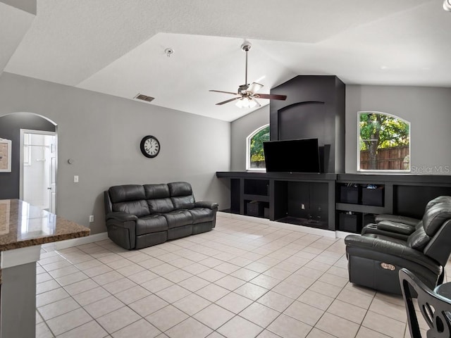 living room featuring a ceiling fan, visible vents, light tile patterned flooring, arched walkways, and vaulted ceiling