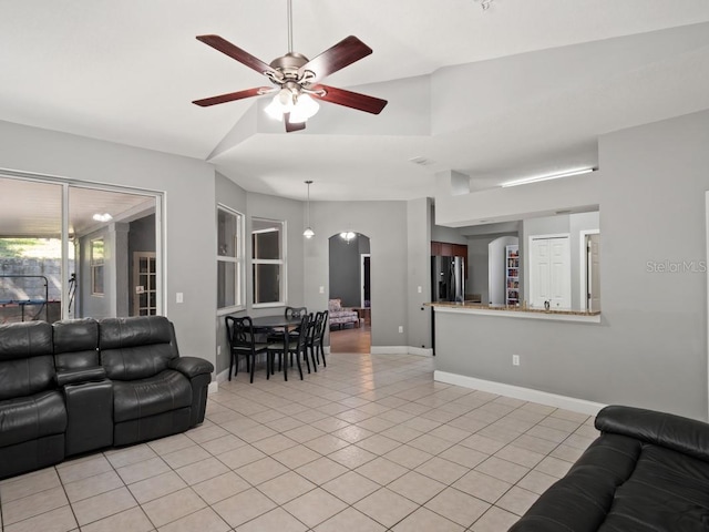 living area featuring ceiling fan, baseboards, lofted ceiling, light tile patterned floors, and arched walkways