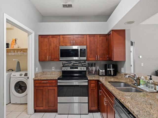 kitchen with visible vents, a sink, light stone counters, stainless steel appliances, and washer / dryer