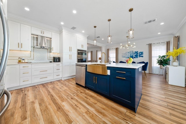 kitchen with visible vents, wall chimney range hood, stainless steel appliances, blue cabinets, and a sink