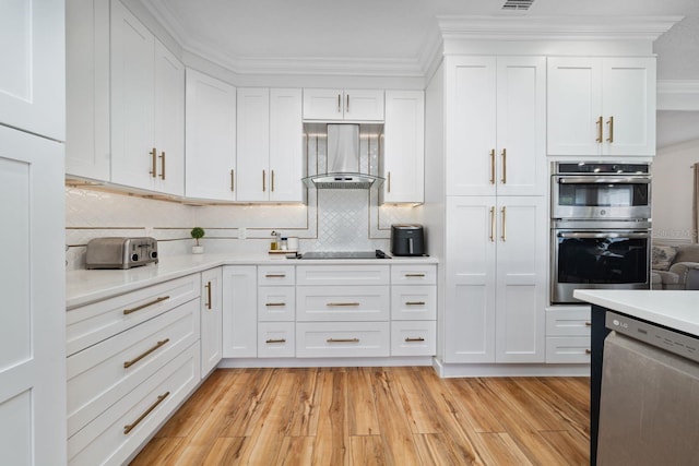 kitchen featuring light wood-style flooring, light countertops, white cabinets, appliances with stainless steel finishes, and wall chimney range hood