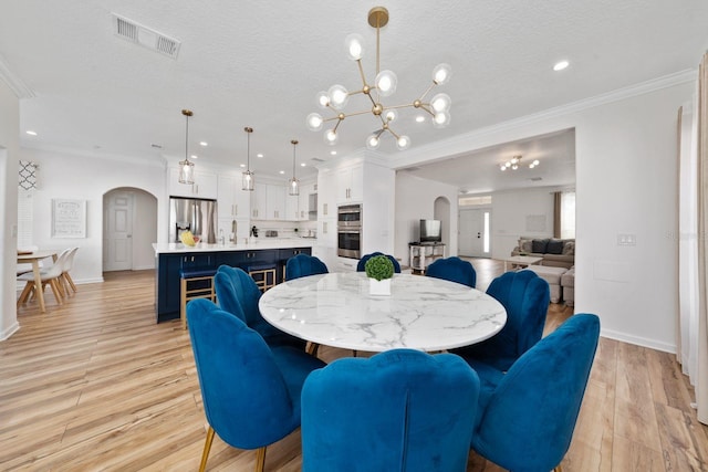 dining area with visible vents, light wood-style flooring, arched walkways, ornamental molding, and a textured ceiling