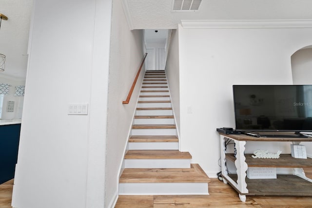 stairway featuring arched walkways, visible vents, wood finished floors, and ornamental molding