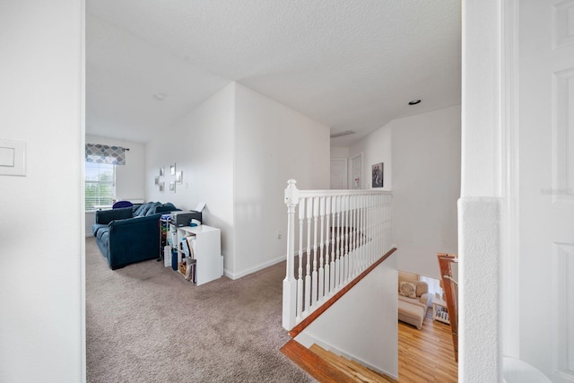 hall with baseboards, an upstairs landing, carpet, and a textured ceiling