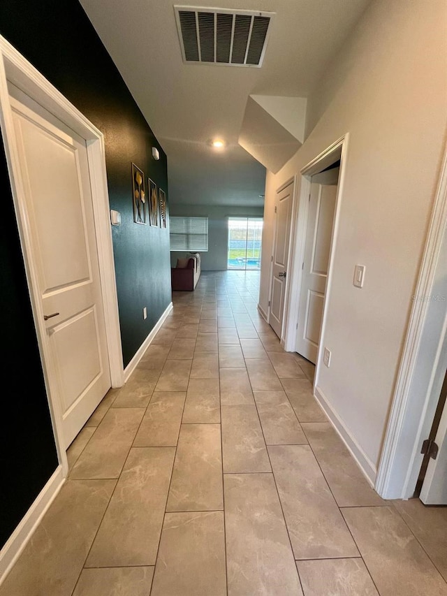 hallway featuring light tile patterned floors, baseboards, and visible vents