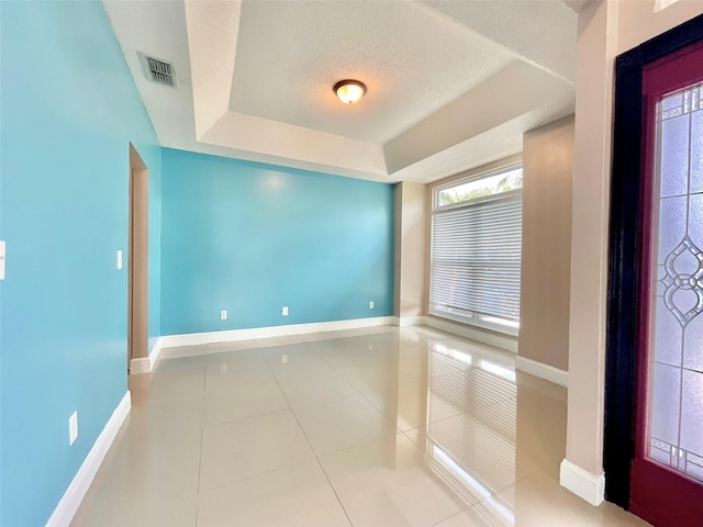 tiled foyer with visible vents, a raised ceiling, and baseboards