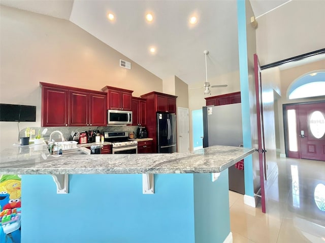 kitchen with a peninsula, a sink, appliances with stainless steel finishes, a kitchen breakfast bar, and reddish brown cabinets