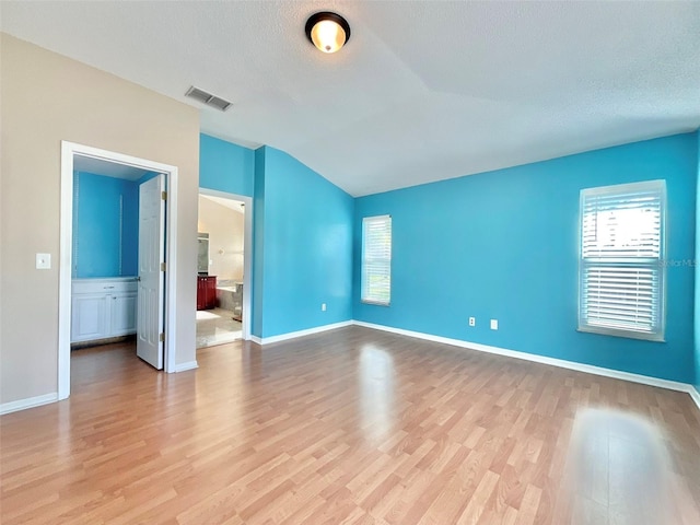 empty room with light wood finished floors, visible vents, baseboards, lofted ceiling, and a textured ceiling