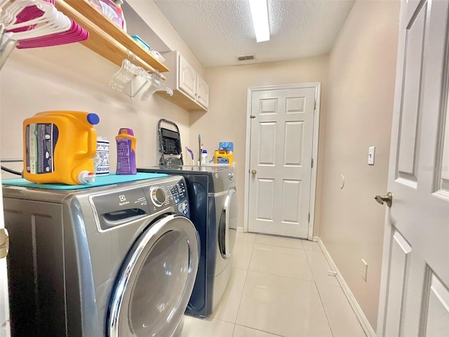 clothes washing area featuring washing machine and clothes dryer, visible vents, light tile patterned floors, cabinet space, and a textured ceiling