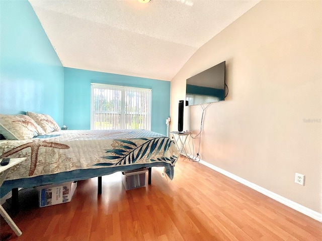 bedroom featuring lofted ceiling, wood finished floors, baseboards, and a textured ceiling