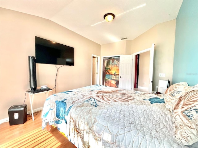 bedroom with visible vents, baseboards, vaulted ceiling, wood finished floors, and a closet