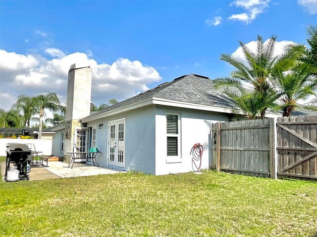 back of property featuring fence, stucco siding, french doors, a lawn, and a patio