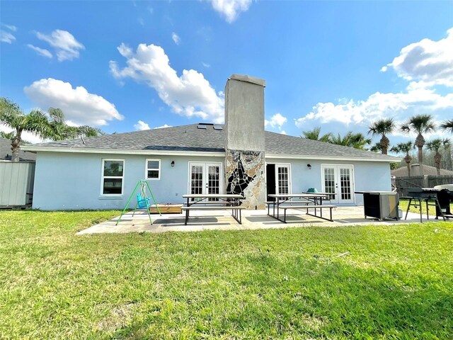 rear view of house featuring a patio, a chimney, stucco siding, french doors, and a lawn