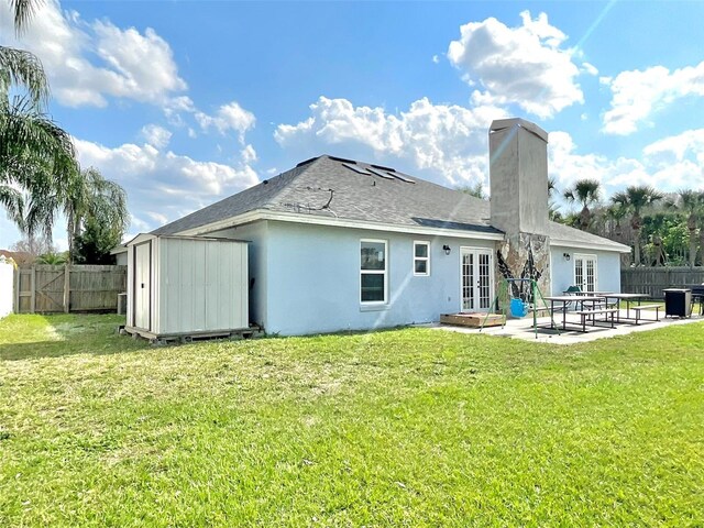 back of house with french doors, a yard, a fenced backyard, a storage unit, and a patio