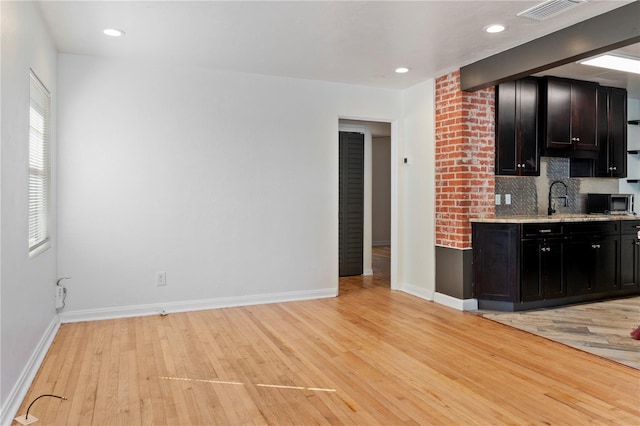 kitchen featuring visible vents, backsplash, baseboards, light wood-type flooring, and a sink