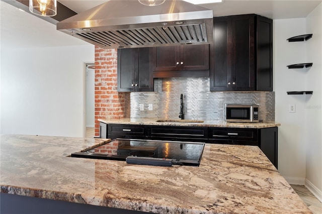 kitchen featuring light stone counters, island exhaust hood, a sink, stainless steel microwave, and backsplash