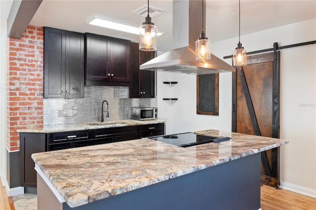 kitchen featuring a barn door, island exhaust hood, a sink, stainless steel microwave, and black electric cooktop