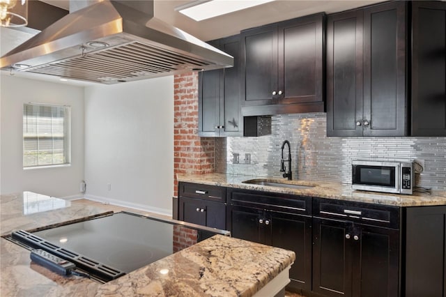 kitchen with light stone countertops, island exhaust hood, a sink, decorative backsplash, and stainless steel microwave