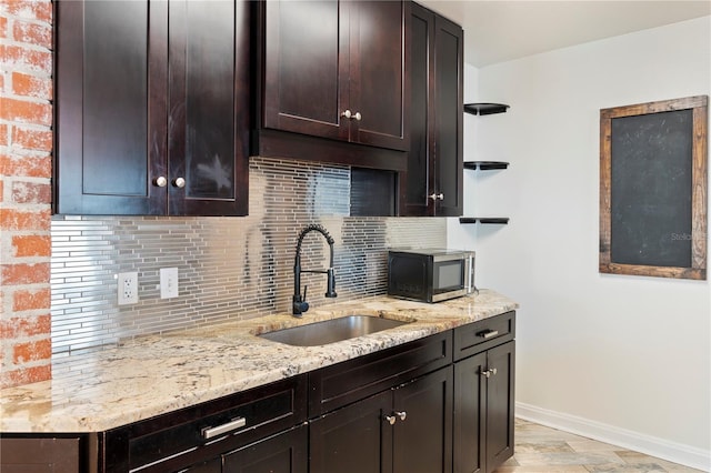 kitchen featuring tasteful backsplash, stainless steel microwave, dark brown cabinets, a sink, and open shelves