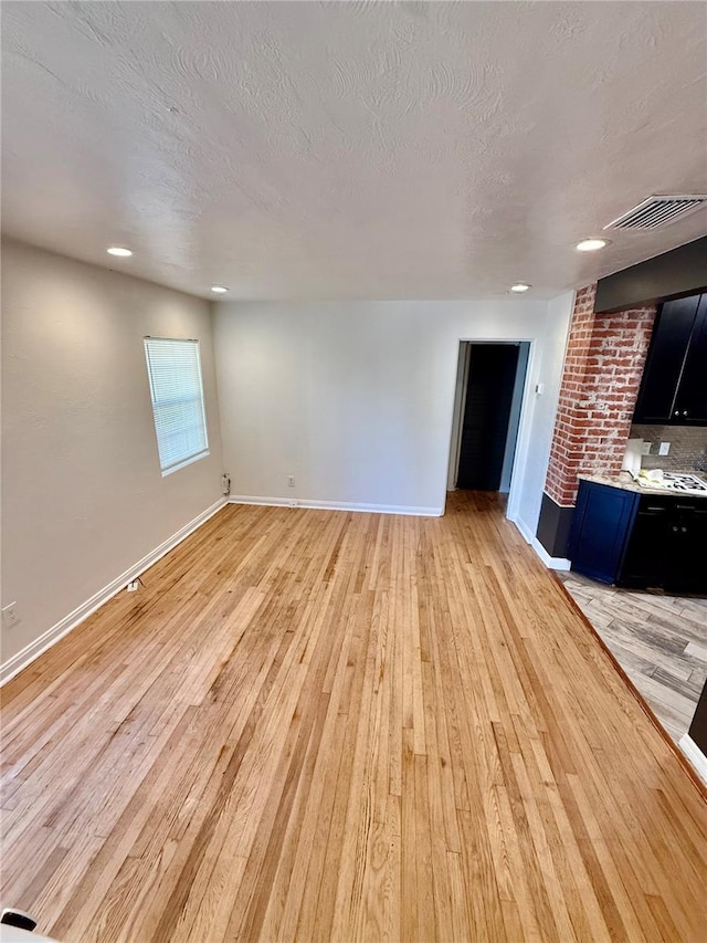 unfurnished living room with light wood finished floors, visible vents, a textured ceiling, and baseboards