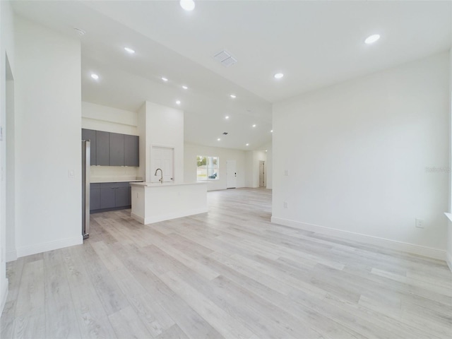 unfurnished living room with visible vents, a sink, recessed lighting, light wood-style floors, and baseboards