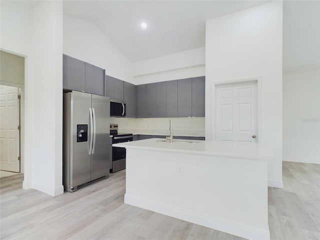 kitchen with light wood-style flooring, an island with sink, a sink, stainless steel appliances, and light countertops