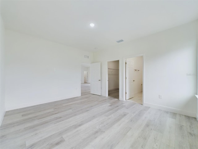 unfurnished bedroom with baseboards, visible vents, light wood-style flooring, a closet, and a walk in closet