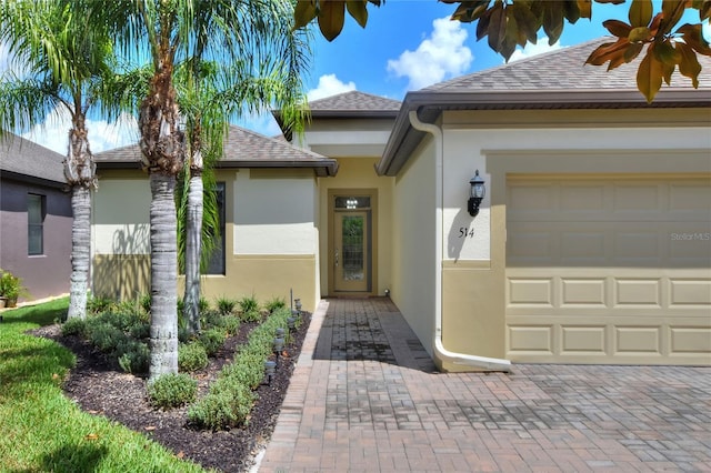 entrance to property with a garage, a shingled roof, and stucco siding