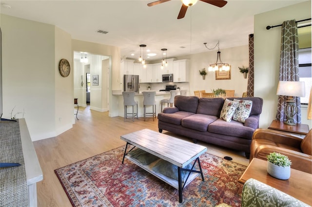 living area with visible vents, baseboards, ceiling fan, and light wood finished floors