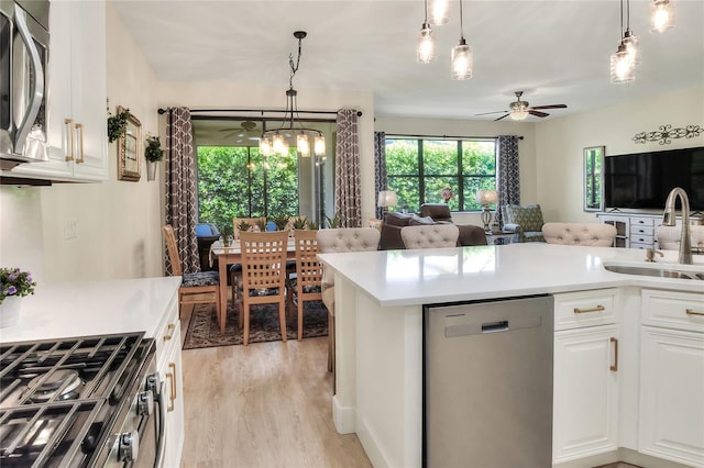 kitchen featuring a sink, appliances with stainless steel finishes, white cabinetry, ceiling fan with notable chandelier, and open floor plan