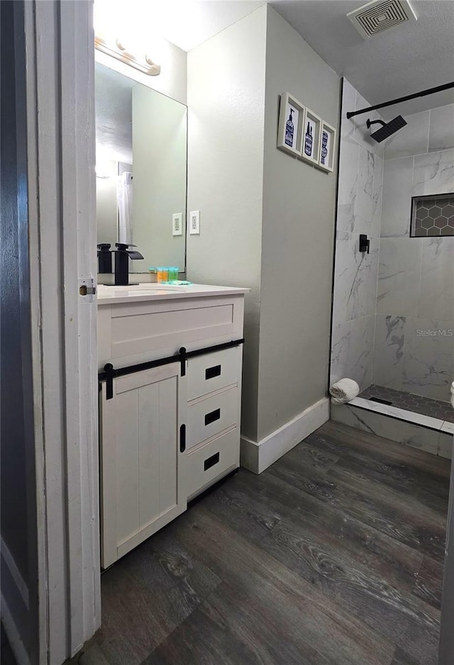 full bathroom featuring visible vents, wood finished floors, baseboards, tiled shower, and vanity