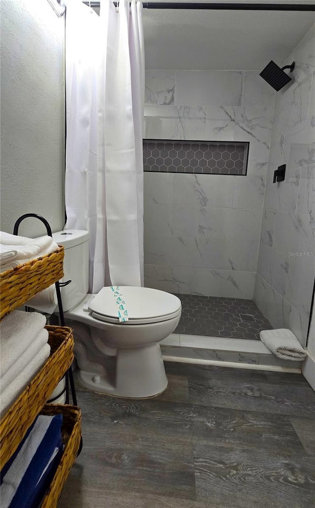 bathroom with tiled shower, toilet, and wood finished floors