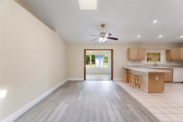 kitchen featuring light brown cabinets, light countertops, a peninsula, a kitchen breakfast bar, and white dishwasher