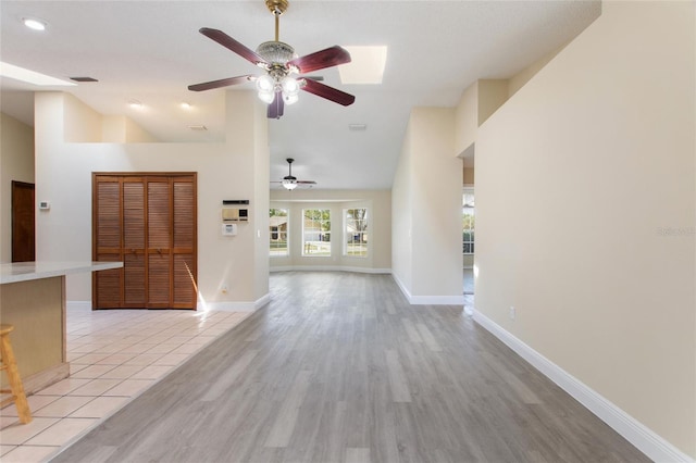 unfurnished living room with light tile patterned floors, high vaulted ceiling, baseboards, and a ceiling fan