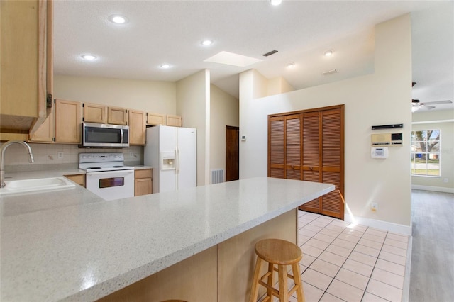 kitchen featuring light brown cabinetry, a sink, white appliances, a peninsula, and vaulted ceiling