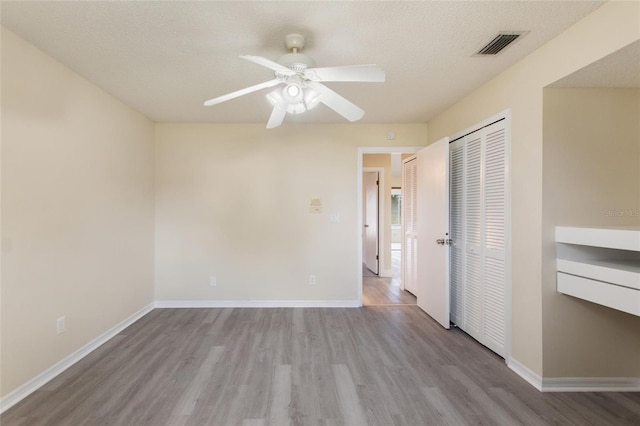 unfurnished bedroom featuring wood finished floors, baseboards, visible vents, a closet, and a textured ceiling