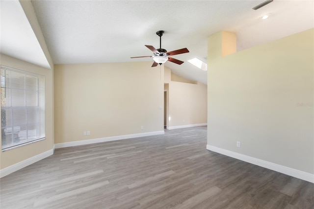 spare room featuring lofted ceiling with skylight, wood finished floors, a ceiling fan, and visible vents