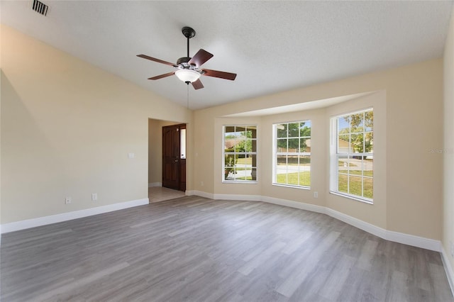 spare room featuring wood finished floors, a ceiling fan, visible vents, baseboards, and lofted ceiling