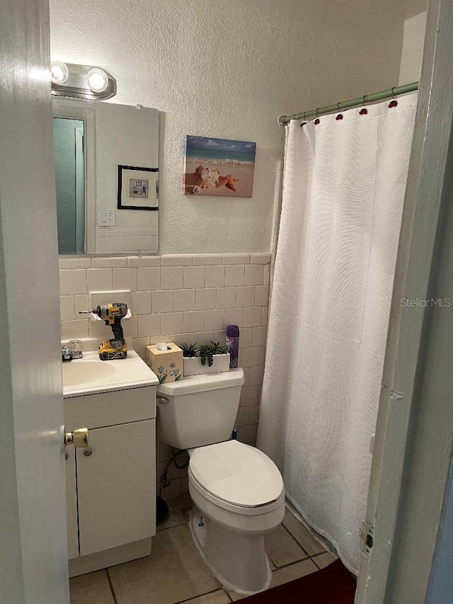 full bath featuring toilet, vanity, a textured wall, tile patterned floors, and tile walls