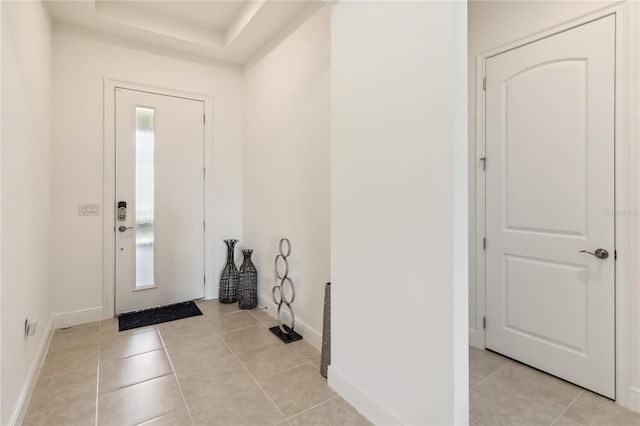 foyer entrance featuring a raised ceiling, light tile patterned flooring, and baseboards