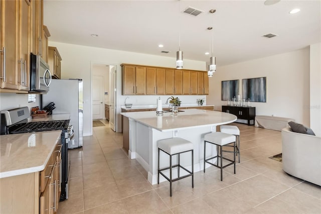 kitchen featuring visible vents, an island with sink, brown cabinets, appliances with stainless steel finishes, and a kitchen breakfast bar