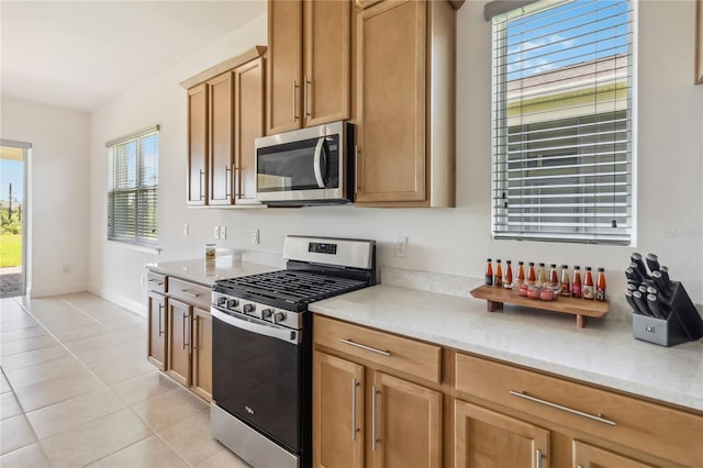 kitchen featuring light tile patterned floors, brown cabinetry, baseboards, light countertops, and appliances with stainless steel finishes