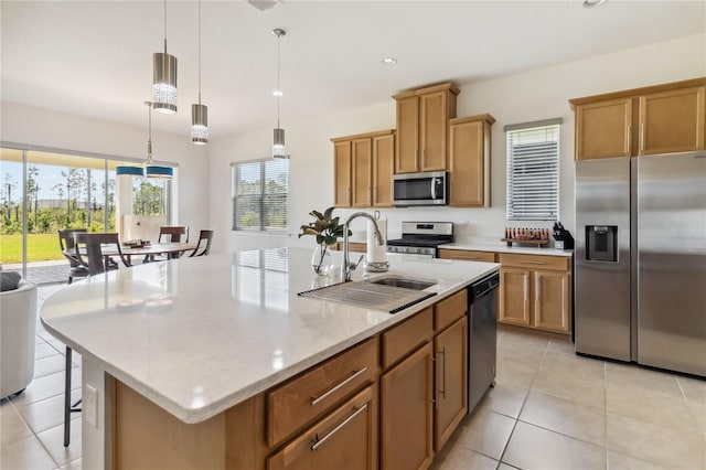 kitchen featuring an island with sink, a sink, stainless steel appliances, light tile patterned flooring, and brown cabinetry