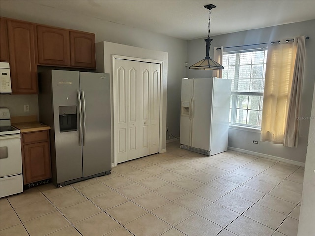 kitchen with brown cabinetry, light tile patterned floors, white appliances, and decorative light fixtures