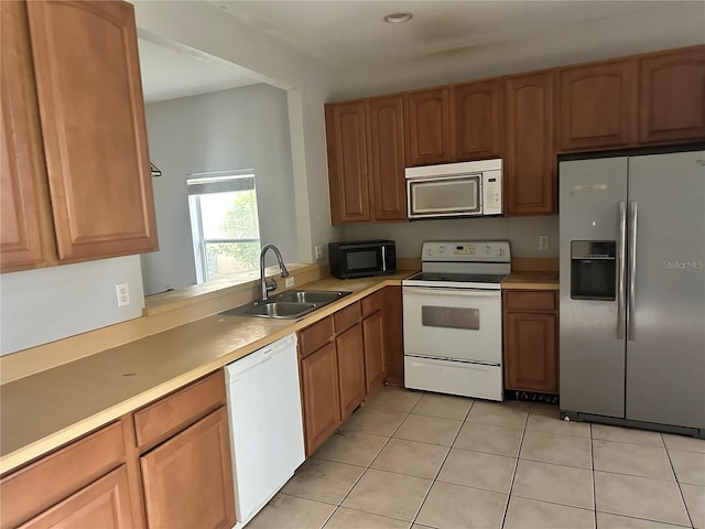 kitchen with light countertops, light tile patterned floors, brown cabinetry, white appliances, and a sink