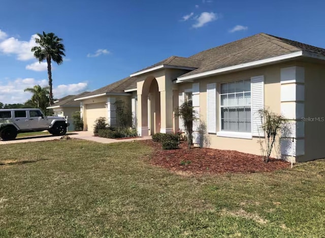 view of front facade with stucco siding, an attached garage, driveway, and a front lawn