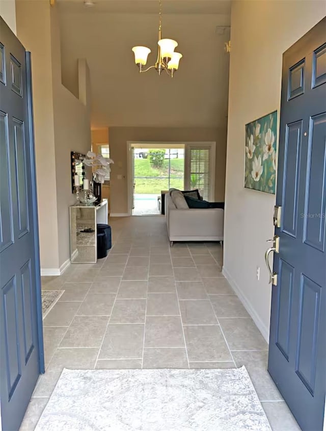 foyer entrance featuring light tile patterned floors, baseboards, a chandelier, and a towering ceiling